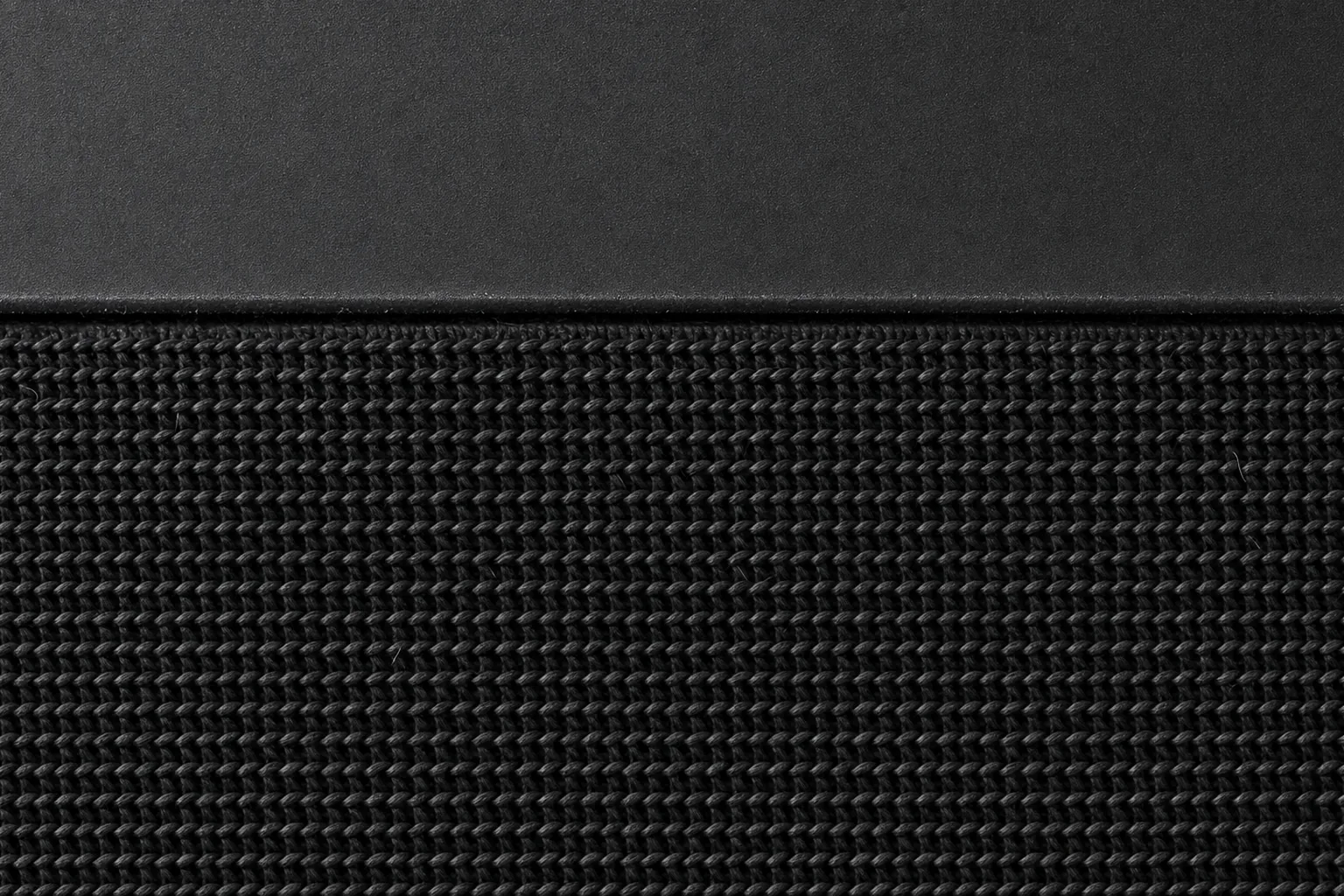 AI-generated concept render of the Nolaka Station, built on our CAD — a macro view of the acoustic knit filling the frame, its ribbed weave running edge to edge, with the seam where the matte charcoal shell meets it crossing the upper third.